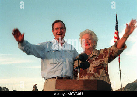 President George Bush and First Lady Barbara Bush wave as they stand in the back of a vehicle during a visit to a desert encampment.  The president and his wife are paying Thanksgiving Day visits to U.S. troops who are in Saudi Arabia for Operation Desert Shield.  Sen. Robert Dole of Kansas is at left. Stock Photo