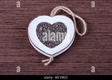 White wood heart shaped frame filled with chia seeds, on brown wood. Stock Photo