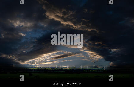 Wind farm with dramatic stormy clouds lighting the wind turbines landscape Stock Photo