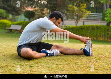 Young guy doing stretching exercise in a park Stock Photo