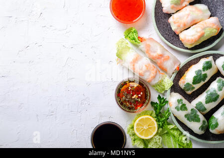 Fresh Vietnamese, Asian, Chinese food frame on white concrete background. Spring rolls rice paper, lettuce, salad, vermicelli, noodles, shrimps, fish  Stock Photo