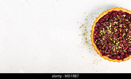 Delicious homamade cranberry, cherry tart with pistachios, powdered sugar on white concrete background for Christmas. Top view. Handmade with love Stock Photo