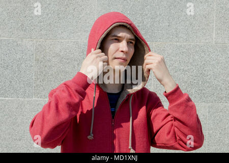 the guy in the red hoodie and stands by the wall and looks to the side. Stock Photo