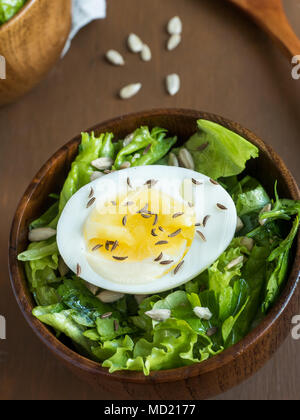 Salad of lettuce leaves and eggs in wooden bowls seeds cumin loaves Dark background. Stock Photo