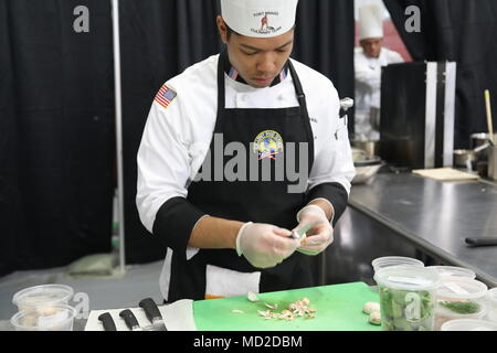 A U.S. Army private first class assigned to Fort Bragg, North Carolina, serves as a culinary arts specialist participating in the 43rd annual Joint Culinary Training Exercise at Fort Lee, Virginia, in March. The archival image records the soldier slicing mushrooms during the student team event while preparing a three-course meal evaluated under American Culinary Federation standards. Stock Photo