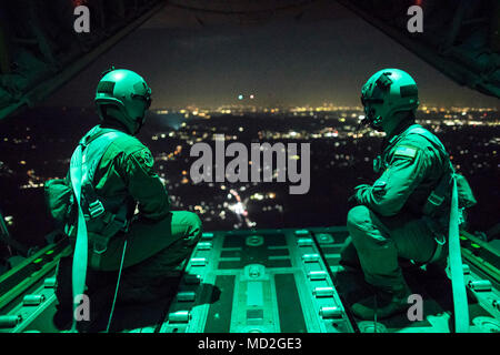 (Left to right) Senior Airman Stephen Clark and Airman 1st Class Matthew Pfeffer, 36th Airlift Squadron C-130J loadmasters, sit on the open ramp of a C-130J Super Hercules flying near Yokota Air Base, Japan, March 26, 2018, before conducting a simulated airdrop over Yokota. Yokota aircrews regularly conduct night flying operations to ensure they are prepared for a variety of contingencies throughout the Indo-Asia Pacific region. Stock Photo