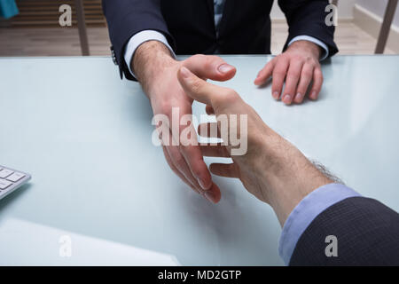 Close-up Of Two Businesspeople Shaking Hands At Workplace Stock Photo