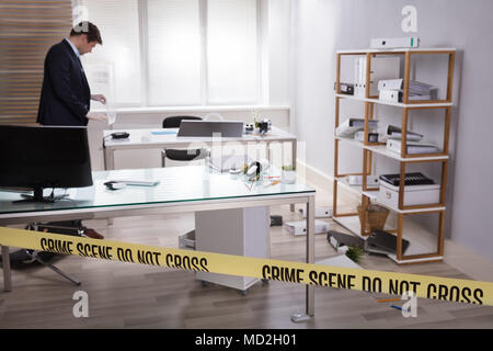 Investigator Collecting Evidence In Office Behind Yellow Crime Scene Tape Stock Photo
