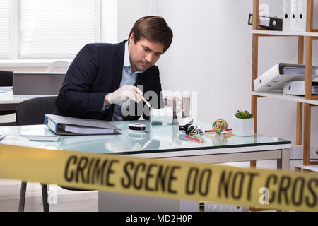 Forensic Expert Searching For Crime Evidence On Pencil Holder Behind Crime Scene Tape Stock Photo
