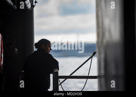 (March 26, 2018) Mass Communication Specialist 3rd Class Lauren Matia Deal, from Houston, Texas, observes an ammunition offload with the aircraft carrier USS Abraham Lincoln (CVN 72) from a weather deck aboard the aircraft carrier USS George H.W. Bush (CVN 77). The ship is underway conducting sustainment exercises to maintain carrier readiness. Stock Photo