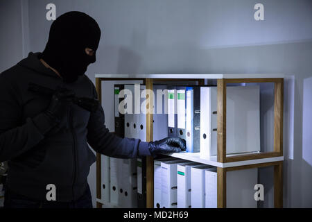 Thief Wearing Balaclava Stealing File From Shelf At Workplace Stock Photo