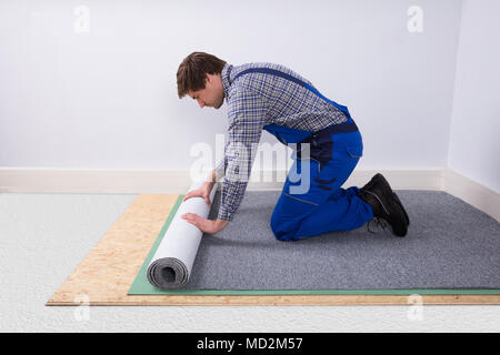 Side View Of A Young Male Worker In Overalls Installing Carpet Stock Photo