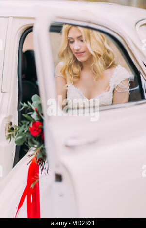 Beautiful blonde bride in white vintage car. Autumn forest on background Stock Photo