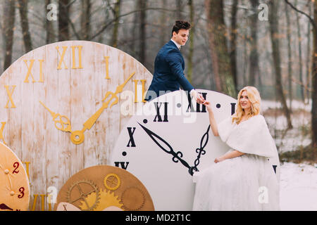 Happy wedding couple softly holding hands at the big vintage clocks in  autumn forest. Creative decorations Stock Photo