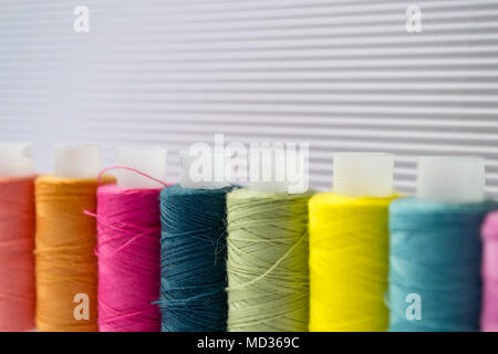 Various colored threads with clothes buttons on white cardboard background. Stock Photo