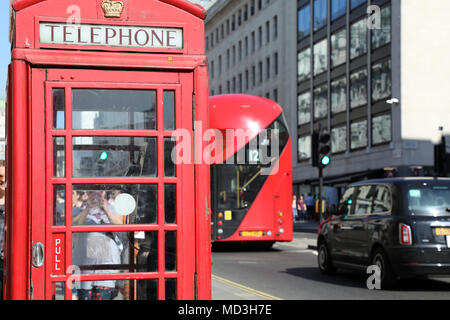 London, UK. 18th April 2018. A red telephone box on Waterloo Place, central London, with a traditional red London bus and a black London taxi driving past, on 18 April, 2018 Credit: Dominic Dudley/Alamy Live News Stock Photo