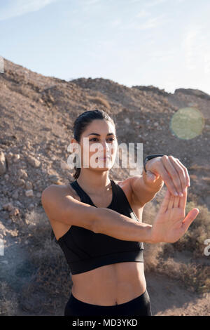 Young female runner stretching arms in arid landscape Stock Photo