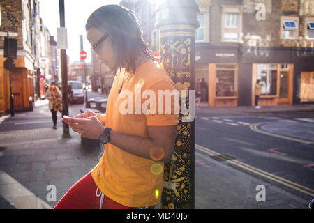 Young man in street, leaning against lamppost, using smartphone Stock Photo