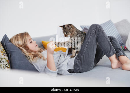 Young girl lying on sofa, playing with pet cat Stock Photo