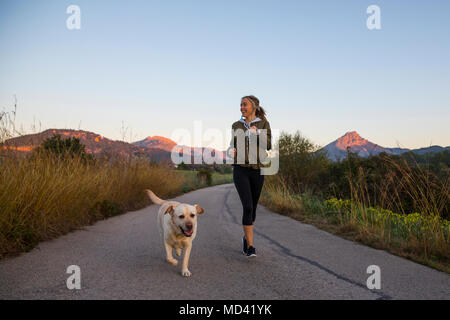 Young woman running along rural road with pet dog Stock Photo