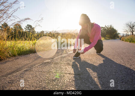 Young woman exercising outdoors, tying shoelace Stock Photo