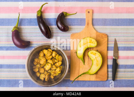 Aubergines, with sliced aubergine on chopping board and pan with prepared food Stock Photo