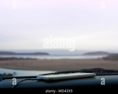 Smartphone on car dashboard, coastal view seen through car windscreen, Broulee, New South Wales, Australia Stock Photo