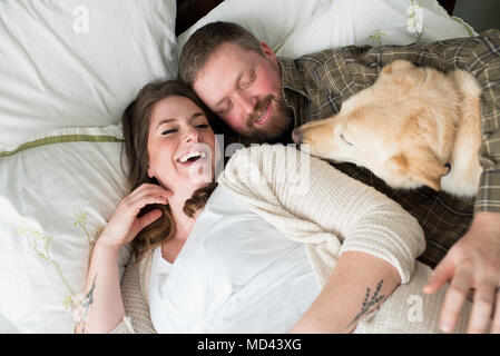 Pregnant woman lying with partner on bed, dog lying on bed beside them, elevated view Stock Photo