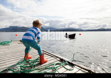 Boy on pier pulling fjord boat by rope, Aure, More og Romsdal, Norway Stock Photo