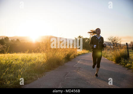 Young woman running along rural road Stock Photo