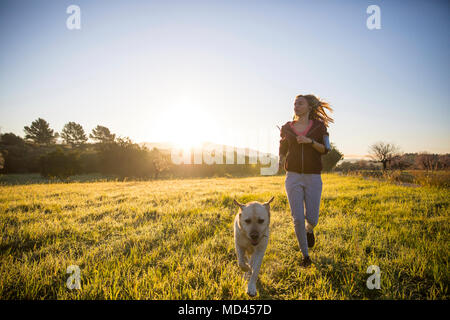 Young woman running across field, with pet dog Stock Photo