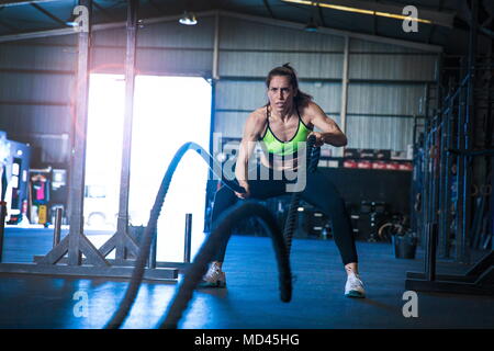Woman exercising in gym, using battle ropes Stock Photo