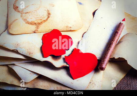 Stack old papers, notebook, wooden pencil and two vintage red hearts on burlap, sackcloth background. Retro design effects Stock Photo