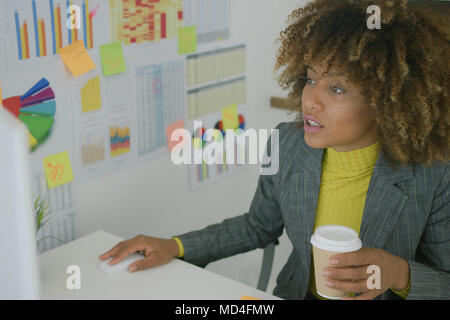 Young worker having coffee while using computer Stock Photo