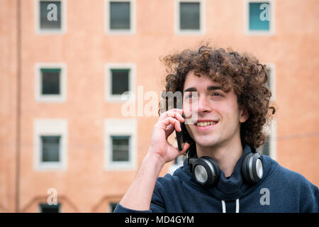 Portrait of handsome young man with curly hair and headphones talking on his mobile phone Stock Photo