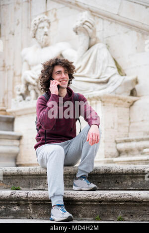 Handsome young man with curly hair in tracksuit talking on his mobile phone in front of Nile God statue in Rome Stock Photo
