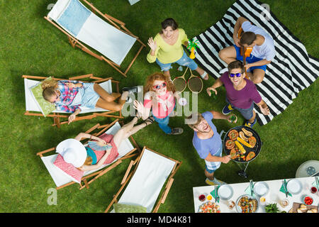 A group of friends looks up and smiles while grilling and having fun on the grass Stock Photo