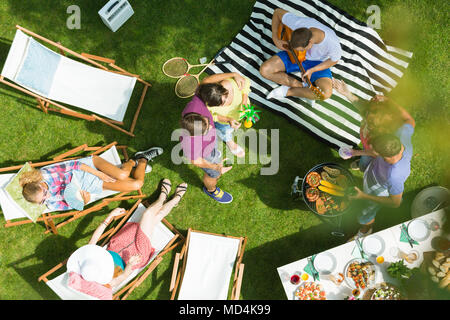 Woman and a man drinking and eating while relaxing with friends on the grass in the park Stock Photo