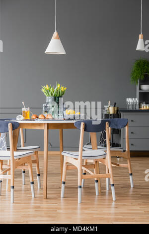 Pastries and honey jar on a minimalist, wooden kitchen table and a modern, white and navy blue chairs in a dark dining room interior with gray walls Stock Photo