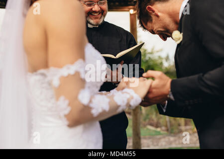 Couple holding hands with groom acknowledging the consent before the priest. Close up of bride and groom during outdoor wedding ceremony with priest q Stock Photo