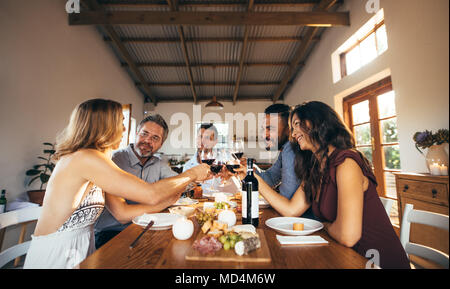 Friends sitting around a table having fun with wine and food. Group of men and women toasting wine at dinner table during party. Stock Photo