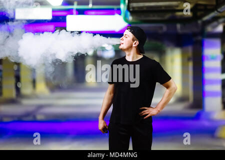 Man in cap smoke an electronic cigarette performing various kind of vaping tricks Stock Photo
