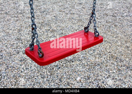 Outdoor public playground equipment metal swing red seat closeup with four holders tied with chain on playground sand background Stock Photo