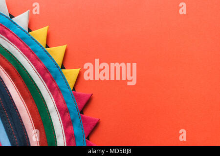 Bright round multicolored handmade striped fabric with a curved triangular edge on red background. Stock Photo