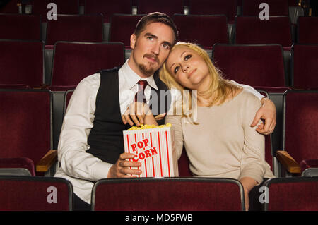 A couple eating popcorn in a movie theater, while watching a movie. Stock Photo