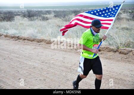 A participant in the 2018 Bataan Memorial Death March races through a checkpoint while displaying an American flag at White Sands Missile Range, N.M., March 25, 2018.  The race was attended by both military and civilian participants from around the world and honored those who defended the Philippines during World War II.  (U.S. Army photo by Pvt. Matthew J. Marcellus) Stock Photo