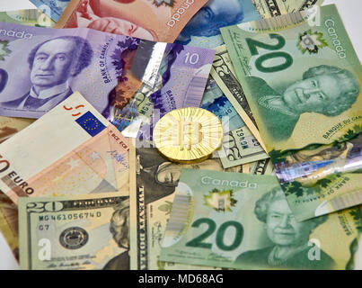 MONTREAL, CANADA - MARCH 10, 2018: Bitcoin cryptocurrency gold coin and logo on euro, american dollars and canadian dollar bank notes. Stock Photo