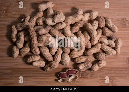 Pile of unshelled natural peanuts in the shell on a natural wooden background top view from above.  One peanut is open with the nuts visible inside. Stock Photo