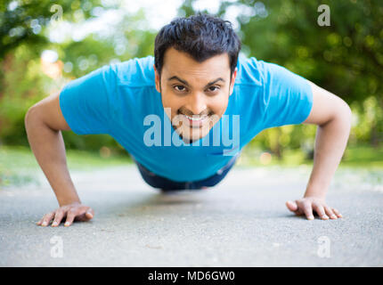 Closeup portrait, young healthy handsome man performing pushup outside on road in park, isolated trees and sky background. Stock Photo
