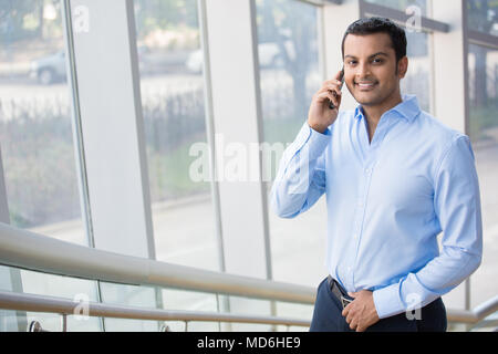 A closeup portrait of a young busy, happy, smiling business man talking on his phone while walking on the office building staircase, isolated on indoo Stock Photo